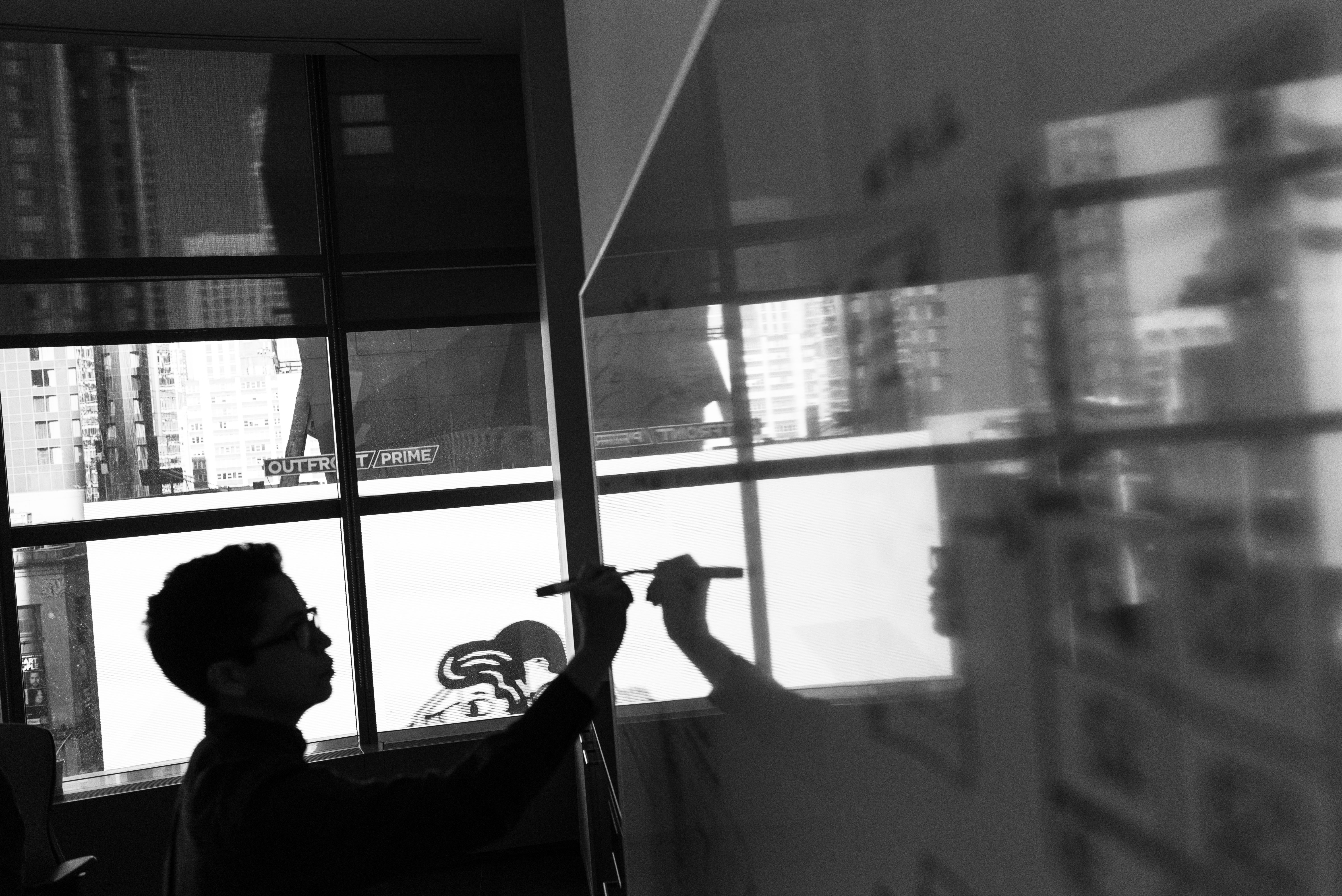 Silhouetted person developing ideas on a glass board.