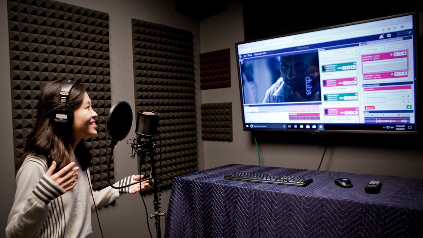 A voice talent recording in a ZOO Digital dubbing studio, with the ZOOdubs recording software running on screen behind her.